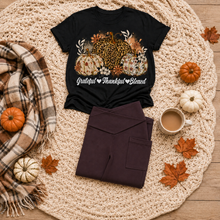 Load image into Gallery viewer, Black crewneck T-shirt featuring leopard and floral pumpkins with white Grateful Thankful Blessed script, styled with folded brown leggings in a fall flat lay.