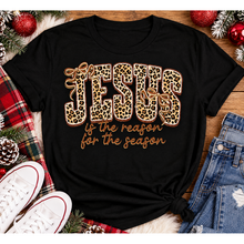 Load image into Gallery viewer, Jesus Is the Reason for the Season Christmas graphic shirt featuring bold leopard print JESUS lettering, decorative gold bows, and gold script. Faith-inspired holiday apparel available in red and black with four style options.