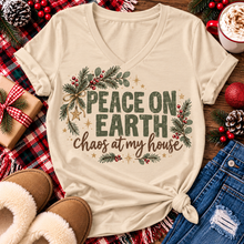 Load image into Gallery viewer, Peace on Earth Chaos at My House funny Christmas graphic apparel featuring distressed olive green lettering, rustic pine greenery, red berries and gold stars, available in sand and sport grey in short sleeve crewneck tees, V-neck tees, sweatshirts and hoodies.