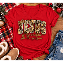 Load image into Gallery viewer, Jesus Is the Reason for the Season Christmas graphic shirt featuring bold leopard print JESUS lettering, decorative gold bows, and gold script. Faith-inspired holiday apparel available in red and black with four style options.
