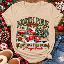 Load image into Gallery viewer, North Pole Christmas Tree Farm vintage holiday graphic shirt featuring a red pickup truck carrying Christmas trees, snowy evergreen trees, rustic farmhouse scenery, festive red bows, and distressed green lettering reading North Pole Christmas Tree Farm Always Fresh. Available in beige and black in short sleeve crewneck, V-neck, long sleeve crewneck, and hoodie styles.