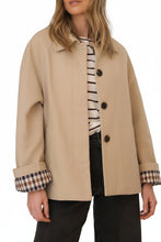 Load image into Gallery viewer, Neutral parchement and plaid short trench coat for your on-the-go customer. Classic plaid lining and folding sleeves, pockets and buttons with hidden placket creates a timeless and versatile look on any body type.