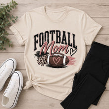 Load image into Gallery viewer, Cream Football Mom graphic T-shirt with distressed black lettering, blush pink accents, leopard print details, and a football with hearts.
