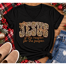Load image into Gallery viewer, Jesus Is the Reason for the Season Christmas graphic shirt featuring bold leopard print JESUS lettering, decorative gold bows, and gold script. Faith-inspired holiday apparel available in red and black with four style options.
