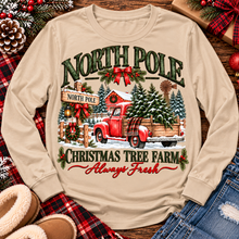 Load image into Gallery viewer, North Pole Christmas Tree Farm vintage holiday graphic shirt featuring a red pickup truck carrying Christmas trees, snowy evergreen trees, rustic farmhouse scenery, festive red bows, and distressed green lettering reading North Pole Christmas Tree Farm Always Fresh. Available in beige and black in short sleeve crewneck, V-neck, long sleeve crewneck, and hoodie styles.
