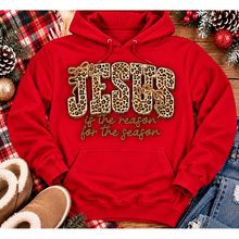 Load image into Gallery viewer, Jesus Is the Reason for the Season Christmas graphic shirt featuring bold leopard print JESUS lettering, decorative gold bows, and gold script. Faith-inspired holiday apparel available in red and black with four style options.
