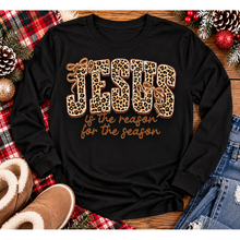 Load image into Gallery viewer, Jesus Is the Reason for the Season Christmas graphic shirt featuring bold leopard print JESUS lettering, decorative gold bows, and gold script. Faith-inspired holiday apparel available in red and black with four style options.
