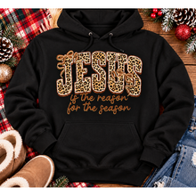 Load image into Gallery viewer, Jesus Is the Reason for the Season Christmas graphic shirt featuring bold leopard print JESUS lettering, decorative gold bows, and gold script. Faith-inspired holiday apparel available in red and black with four style options.
