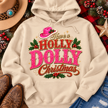 Load image into Gallery viewer, Have a Holly Dolly Christmas western graphic shirt featuring pink and red glitter-inspired lettering, a festive pink cowgirl hat, gold accents, and Christmas holly berries. Available in beige and pink in short sleeve crewneck, V-neck, long sleeve crewneck, and hoodie styles.
