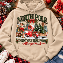 Load image into Gallery viewer, North Pole Christmas Tree Farm vintage holiday graphic shirt featuring a red pickup truck carrying Christmas trees, snowy evergreen trees, rustic farmhouse scenery, festive red bows, and distressed green lettering reading North Pole Christmas Tree Farm Always Fresh. Available in beige and black in short sleeve crewneck, V-neck, long sleeve crewneck, and hoodie styles.
