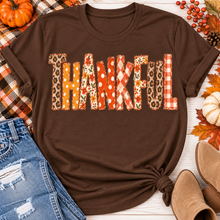 Load image into Gallery viewer, Brown short sleeve crewneck graphic tee with Thankful lettering in orange and neutral fall patterns, styled with distressed jeans.
