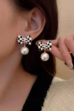 Load image into Gallery viewer, Close-up of a person wearing bow-shaped earrings with pearl drops.
