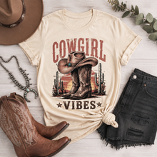 Load image into Gallery viewer, Cream Cowgirl Vibes graphic tee featuring vintage cowboy boots, western hat, cactus and desert sunset design in rustic brown and red tones.

