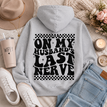 Load image into Gallery viewer, Gray graphic hoodie featuring bold black “On My Husband’s Last Nerve” lettering with checkerboard and sparkle details on the back.

